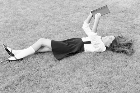 Achieving Excellence. small girl reading book. literature for kids. write childhood memories. her diary. making notes in notebook. back to school. kid study in park. relax on green grass with bookの写真素材