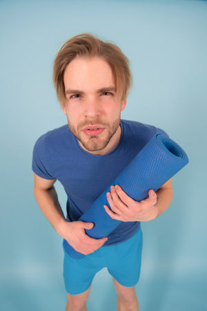 Sportsman look with serious face. Man hold yoga mat. Fashion athlete in blue tshirt and shorts. Gym equipment for training and workout. Yoga or pilates and sport activityの写真素材