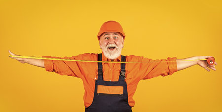 Confident mechanic. happy carpenter. handyman measuring wall. senior builder tape-line for measure. measurement. engineer size measuring. Construction man hold measuring tape. engineering and repairの写真素材
