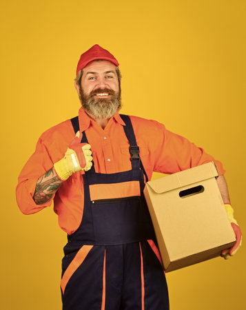 Higher Quality of Living. move to new apartment. bearded loader in uniform. Cardboard boxes - moving to a new house. purchase of new habitation or repair of room. Man wearing boilersuit packing boxesの写真素材