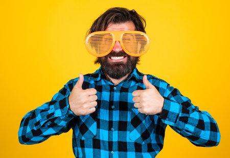 bearded man in funny glasses. brutal guy wear checkered shirt. male with moustache having fun. handsome hipster party goer. happy mature man showing thumb upの写真素材