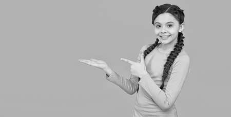 stylish braids and pigtails. copy space. teenage girl presenting product. professional hairdo. kid fashion and beauty. small girl after hairdresser. childhood happiness. beautiful braided long hairの写真素材