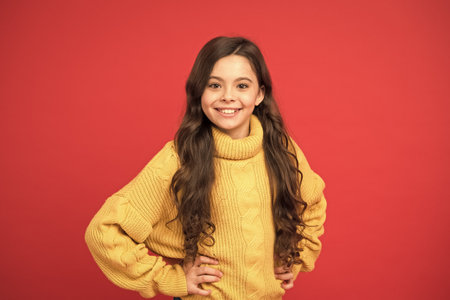 pretty girl long curly hair. childhood happiness. happy little girl knitted sweater. fashion for...