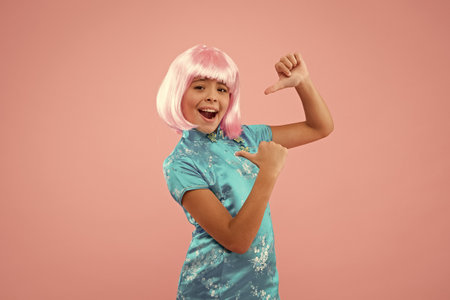 small chinese girl in pink wig. Beauty look of small fashion model. Creating fancy look. Small child pink background. Pointing gesture. kid in traditional Chinese gown. asian cultureの写真素材