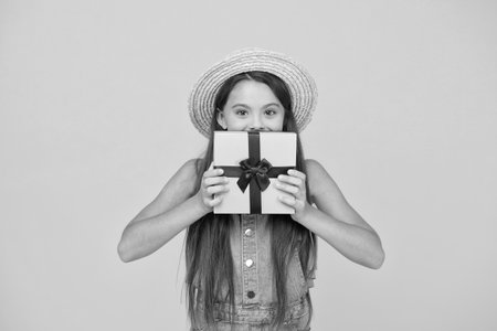 Design your own box. Little girl hold gift box yellow background. Holiday celebration. Birthday anniversary. Wrapped box or package. Gift shop. Shopping. Present delivery. Tie ribbon around boxの写真素材