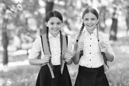 Playful mood. Fashion little girls with backpack in park. children with backpack smiling. students outside in summer park smiling happy. girls with school bags. child with backpack. happy timeの写真素材