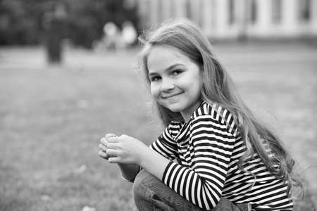Happy child sit on haunches outdoors. Little girl child in casual style. Fashion trend. Trendy style. Childcare and childhood. International childrens dayの写真素材