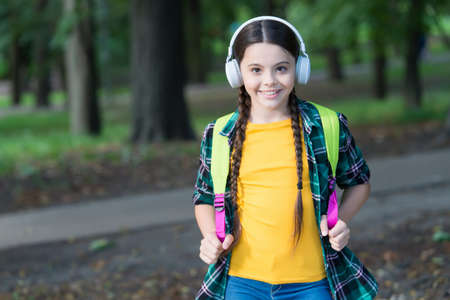 Happy kid listen to audio course in modern headphones carrying school bag in casual fashion style...