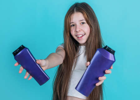 cheerful kid girl with long straight hair hold conditioner shampoo or gel bottle, hygieneの写真素材