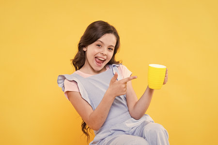 Drink it baby. Happy child point finger at cup yellow background. Little kid enjoy hot drink. Milk tea. Hot cacao or chocolate. Tasty drink recipe. Natural nutrition. Healthy dieting. Lets drink itの写真素材