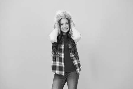 Add some personality to cold weather wardrobe. Happy child wear faux fur hat. Little girl smile in hat yellow background. Fluffy and warm trapper hat for kid. Fashion hat for outdoor adventuresの写真素材