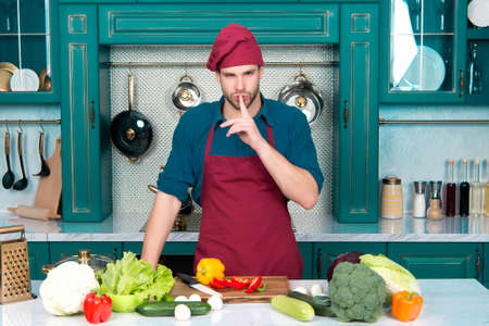 Man cook secret dish in kitchen. Chef with silence gesture finger at table with vegetables....