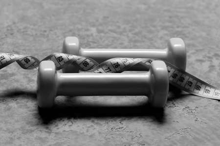Dumbbells made of cyan plastic on grey texture background. Pair of barbells and twisted measure tape, close upの写真素材