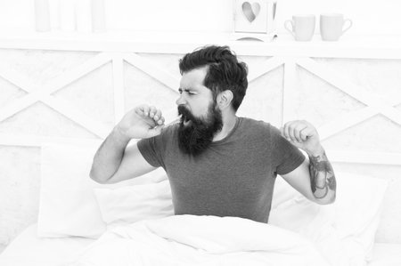 relaxed yawning man waking up in the morning in bed at home, lazy sundayの写真素材
