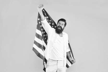 Becoming american citizen. Happy hipster celebrate Independence day. Bearded man hold american flag yellow background. July 4th celebration. American traditions. Democracy and rights. American dreamの写真素材