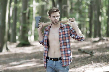 Fit handsome guy with sexy torso in open plaid shirt hold large axe in muscular hands summer wood, strongの写真素材
