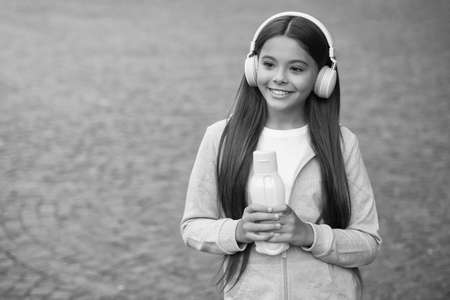 healthy drink for teen. feel thirsty after fitness. girl care body hydration. active and healthy kid drink water. child with juice bottle in earphones. back to school. health care in childhoodの写真素材
