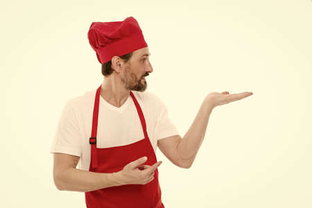 Gesturing aside. Mature chief cook in red cooking apron. Senior cook with beard and moustache...