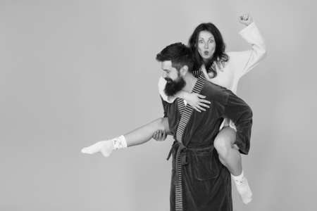 Handsome young man giving his girlfriend piggyback ride. Couple in bathrobes having fun turquoise...