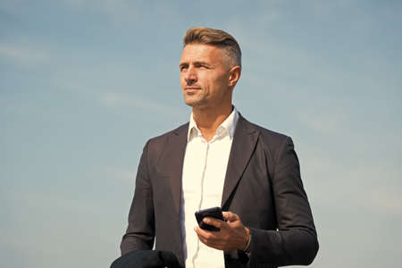 Communicating on the go. Handsome man hold mobile phone outdoors. Business communication. Mobile...