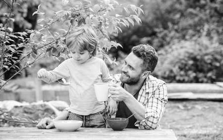 Healthy food concept. Father son eat food and have fun. Menu for children. Family enjoy homemade meal. Food habits. Little boy with dad eating food picnic yard nature background. Summer breakfastの写真素材