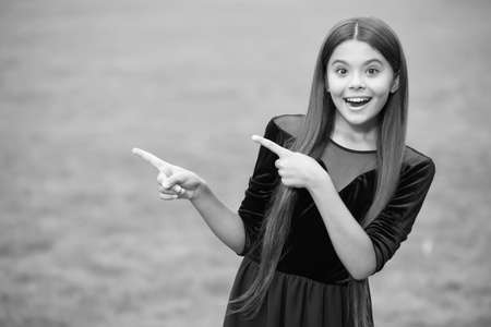 Look at this. Happy girl point index fingers green grass. Objective pointing. Hand gesture. Marketing product or service. Indicating event or location. Pointing for copy spaceの写真素材