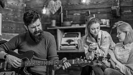 Man with long bushy beard singing passionately, music concept. Girls drinking tea or wine and enjoying lovely tunes. Bearded man playing guitar. Guitarist with hipster beard performing new songの写真素材
