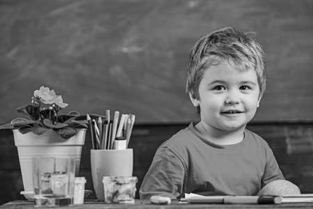 Toddler cute and cheerful ready to study. Kid boy in classroom near flower in pot and pencils,...