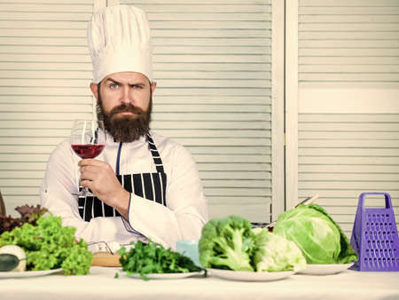 Wine degustation. Match wine and food like expert. Man wear hat and apron enjoy taste drink. Master chef hold glass of wine. Add bit of alcohol. Which wine serve with dinner. Exquisite dinner conceptの写真素材