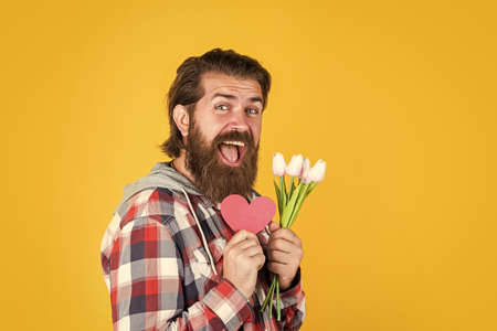valentines day party. happy birthday gift with love. spring bouquet for her. ready for romantic date. present for womens and mothers day. happy bearded man hold tulip flowers and decorative heartの写真素材
