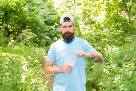 mature bearded man with beard in summer clothes open water bottle in forest, after training