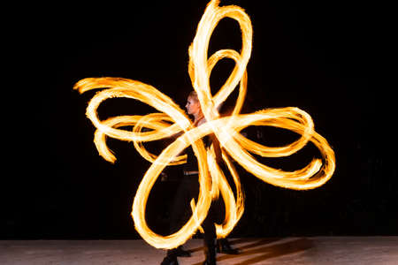 sexy woman artist perform fiery twirly trails by spinning flaming pois during fire performance