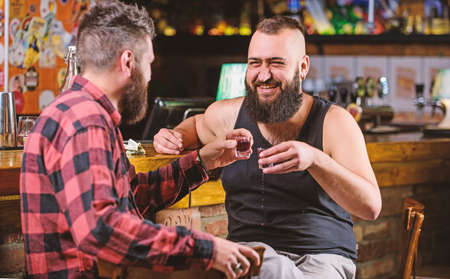Cheers concept. Hipster brutal bearded man drinking alcohol with friend at bar counter. Men drunk relaxing at pub having fun. Strong alcohol drinks. Friday relax in pub. Friends relaxing in pubの写真素材