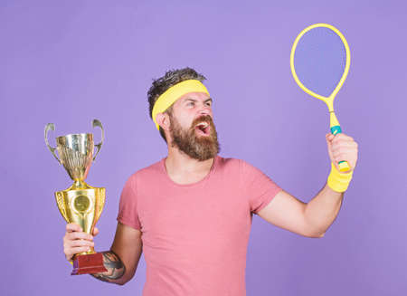 Tennis player win championship. Man bearded successful athlete. First place. Sport achievement. Tennis champion. Win tennis game. Celebrate victory. Athletic man hold tennis racket and golden gobletの写真素材
