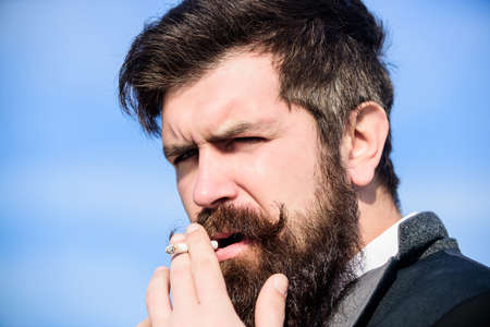 Bearded hipster smoking cigarette sky background. Guy cigarette enjoy nicotine influence. Cigarettes help us with everything from boredom to anger management. Man with beard mustache hold cigaretteの写真素材