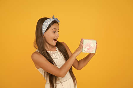 Just starting to enjoy. Happy girl got small gift box. Small child celebrate holidays. Small kid hold present yellow background. Happy birthday. Celebrating anniversary. Holiday celebrationの写真素材