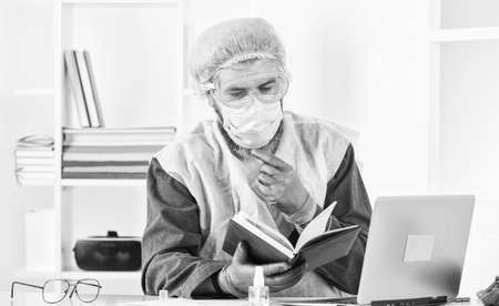 Doctor studying. virus outbreak. Latest scientific findings and knowledge on virus disease. Learn how protect yourself. Man reading book. Medical research. Worker in protective equipmentの写真素材
