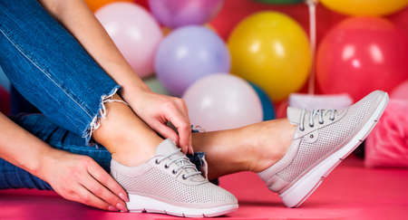female feet in sporty comfortable shoes with laces at colorful balloons, shoe careの写真素材