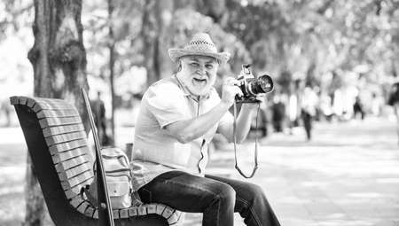 Time to relax. old man relax on bench. man tourist use camera take photo. concept of photography. senior bearded man photographing outdoor. professional photographer designer. happy retirementの写真素材