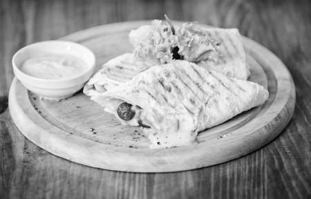 Lavash burrito stuffed meat sausage and cheese sauce served salad. Meat wrapped with lavash burrito. Restaurant meal traditional cuisine. Burrito tortilla served wooden board. Restaurant food conceptの写真素材