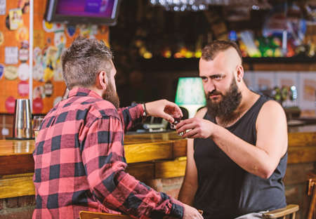 Men relaxing at pub. Strong alcohol drinks. Friday relax in pub. Friends relaxing in pub. Drunk conversation. Cheers concept. Hipster brutal bearded man drinking alcohol with friend at bar counterの写真素材