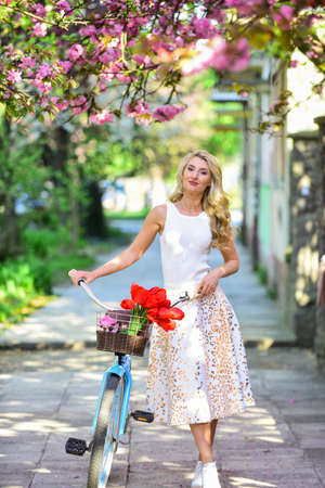 It is spring time. fashion and beauty. woman ride vintage bicycle. romantic girl under sakura blossom. beautiful spring season nature. cherry blooming flowers. pink blossoming sakura. relax in parkの写真素材