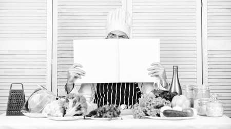 Useful book for cooking. Start culinary career. Ultimate cooking guide step by step. Book recipes copy space. Man chef in hat and apron read book. Culinary recipes book concept. Improve cooking skillの写真素材