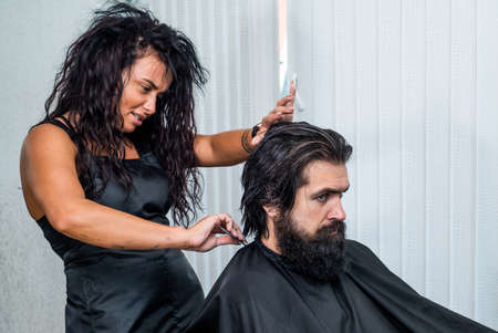 confident brutal guy with barbershop professional master. scissors and brush for hipster. male barber care. bearded man at hairdresser chair in salon. beauty and fashion. hair and beard stylingの写真素材