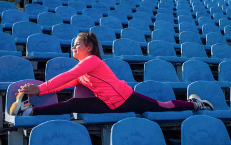 Flexible girl child in sportswear do splits stretching legs on stadium seats, flexibilityの写真素材
