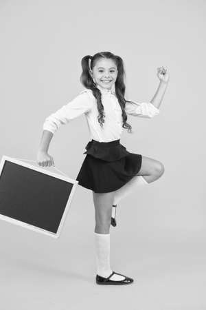 Follow me. Schoolgirl pupil informing. School girl hold blank chalkboard copy space. Announcement and promotion. Girl school uniform hold blackboard going. Back to school concept. Making stepの写真素材