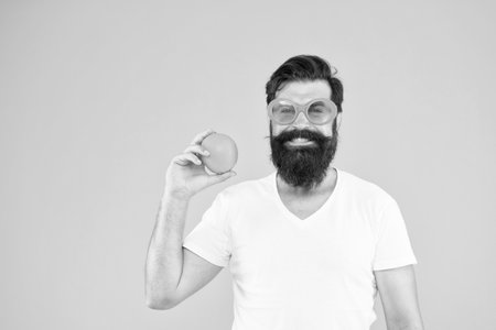 Juicy fruit. Man bearded hipster in orange sunglasses on yellow background. Cheerful guy with ripe fruit. Summer vacation. Fresh and healthy. Summer nutrition. Hipster with beard in summer moodの写真素材