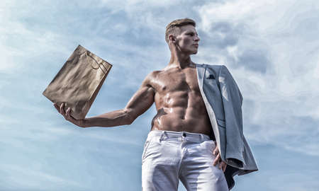 Man muscular athlete hold shopping bag sky background. Hot sales and discount. Guy attractive macho carry shopping bag made out of brown paper. Sales season. Take this package. Shop assistant conceptの写真素材