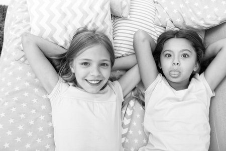 Best friends forever. Girls children lay on bed with cute pillows top view. Pajamas party concept. Girls in playful mood with grimace face. Friends children having fun together and feel comfortableの写真素材