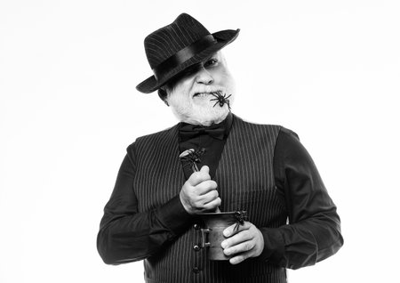 Weird old bartender with gray beard and spider. Preparing magic drink. Halloween concept. Strange people. Elegant bartender wear hat and vest prepare drink. Horror party. Frightening bartenderの写真素材